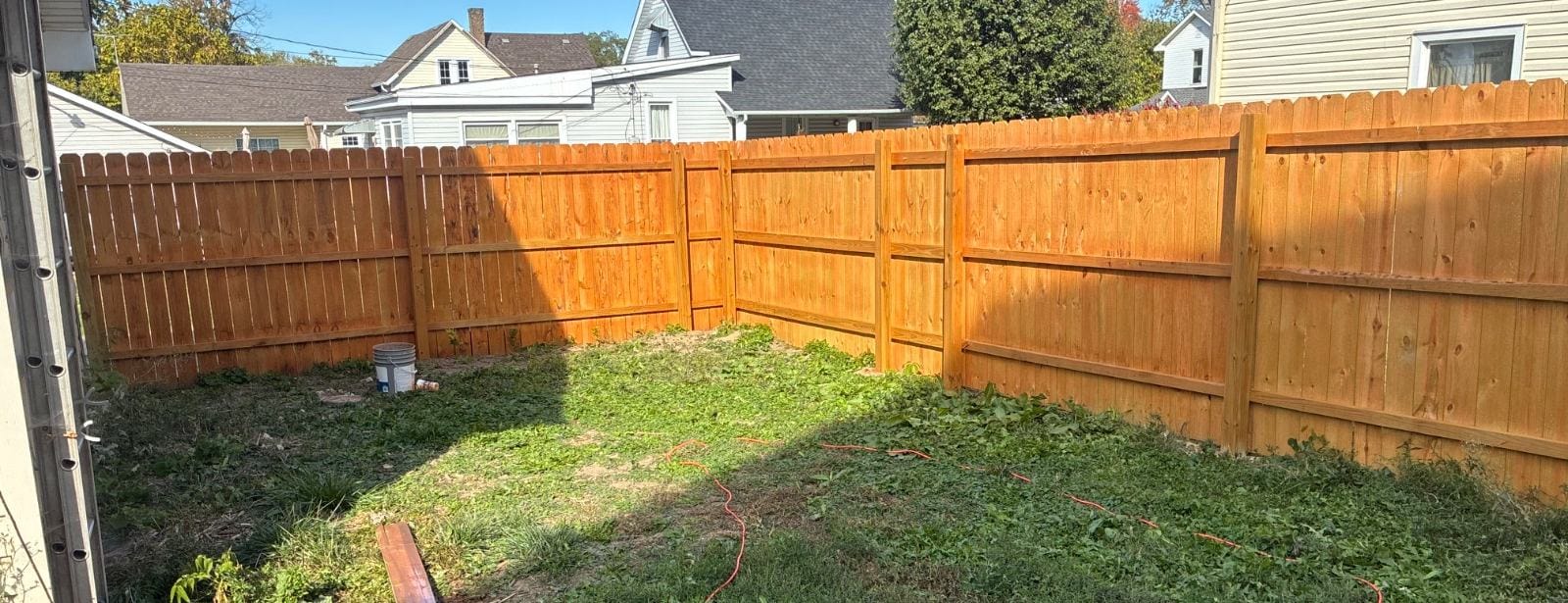 Stained wood privacy fence running along a back yard